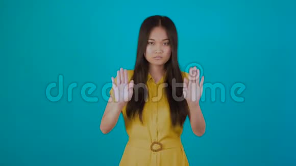 严肃的亚洲女性在4K蓝底镜头上显示停止手势视频的预览图