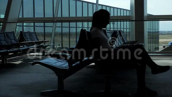 女人正坐在机场空等候厅里浏览智能手机视频的预览图