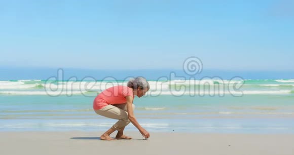 活跃的非洲裔美国妇女在海滩上捡贝壳的侧面景色视频的预览图
