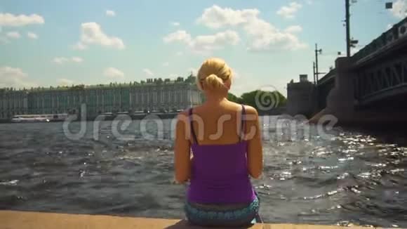 女人坐在河堤上享受美丽的夏日天气视频的预览图