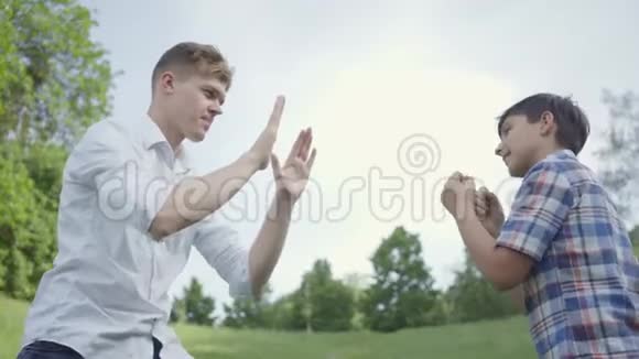 描绘公园里的年轻人和男孩拳击年轻的父亲模仿拳打脚踢他的儿子也这样做家庭视频的预览图