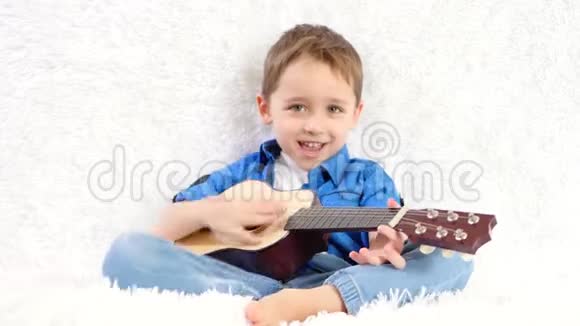 一个孩子高兴地弹着吉他坐在白色沙发上唱歌视频的预览图