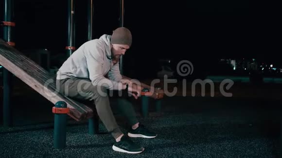 一个人晚上坐在公园里的运动器材上用智能手表视频的预览图