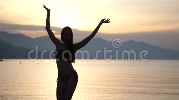年轻苗条的女孩在日落时分穿着泳衣在海滩上慢动作跳舞视频的预览图