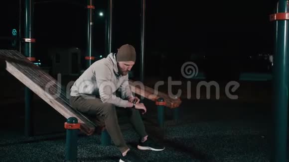 男人晚上坐在公园的运动场上看智能手表视频的预览图