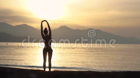 穿着泳衣的女孩在日出时在海边慢动作伸展身体视频的预览图