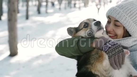 快乐的女人戴着羊毛帽戴着长长的温暖围巾在寒冷的阳光明媚的日子在下雪的冬天公园里抚摸她的宠物快乐视频的预览图