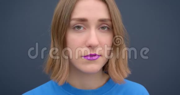 年轻的短发女性的特写镜头涂着紫色口红看着灰色背景的镜头视频的预览图