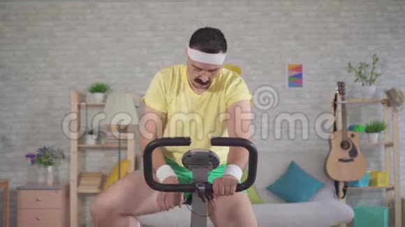 这位80带胡子的有趣运动员在家里骑着运动自行车喝水视频的预览图