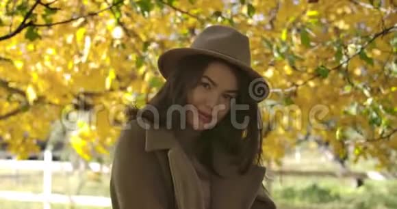 戴帽子的害羞欧洲女孩站在黄叶背景上微笑的肖像白人女性视频的预览图