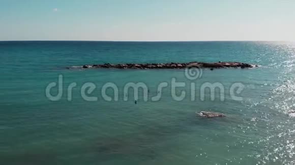 无人机在岩石海岸附近飞行蓝色海水的鸟瞰图美丽的海洋景观年轻有魅力的男人太阳晒黑视频的预览图