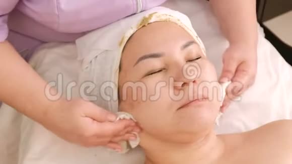 美容师双手用棉垫擦拭皮肤并将海藻酸钠面膜的残留从面部取出视频的预览图