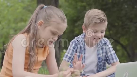 公园里一个英俊的男孩和漂亮的女孩留着长发看着一台笔记本电脑的相机夏季视频的预览图