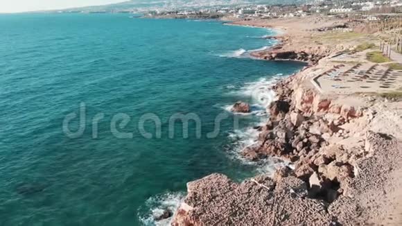 海浪拍打和撞击岩石悬崖海滩岩石海岸的空中景观鸟儿飞过海岸线C型无人机视频的预览图