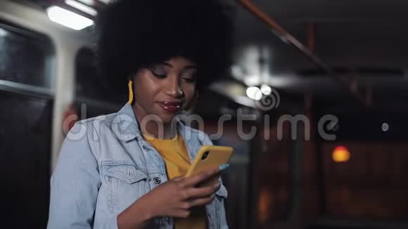 吸引人的是年轻的非裔美国妇女在公共交通中使用智能手机晚上城市灯光背景视频的预览图
