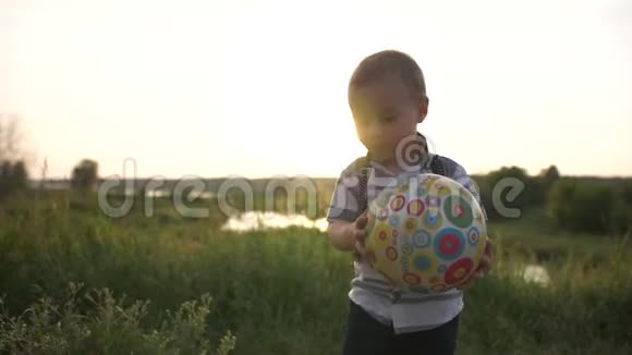 一个可爱的小男孩缓慢地向大自然投掷一个充气球视频的预览图