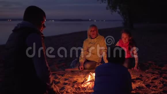 一家人在海滩徒步旅行时父亲在篝火旁抚摸儿子的头视频的预览图