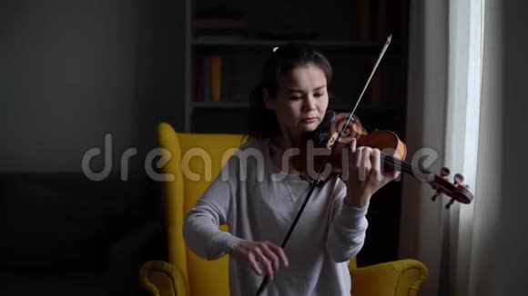 美丽的年轻女子音乐家拉小提琴坐在柔软的椅子上视频的预览图
