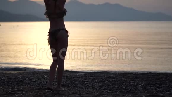 傍晚时分一个身材苗条的高个子女孩穿着泳衣在海滩上慢动作跳舞视频的预览图