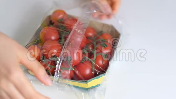 女人用食物胶片在白色桌子上储存食物一次性塑料包装中的樱桃番茄慢动作视频的预览图