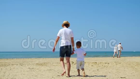 在阳光明媚的日子里妈妈和孩子牵着手沿着海边沙滩散步旅游度假和快乐的概念视频的预览图