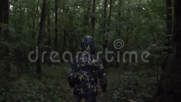 晚上穿着夹克和兜帽的男孩穿过森林视频的预览图