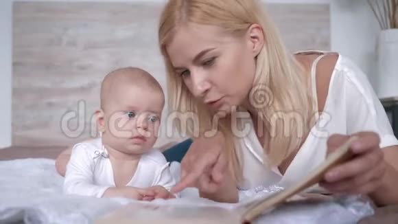 新妈妈给她的小女儿读了一本书小女儿一边躺在家里一边好奇地听着她视频的预览图