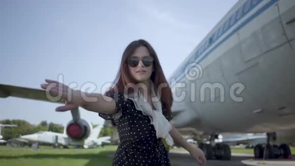 肖像快乐嬉戏的黑发女孩戴着太阳镜在大飞机前看着相机夏天快乐视频的预览图