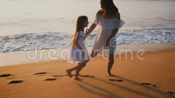 幸福美丽的妈妈和小女儿在夕阳沙滩上一起旋转放松身心视频的预览图