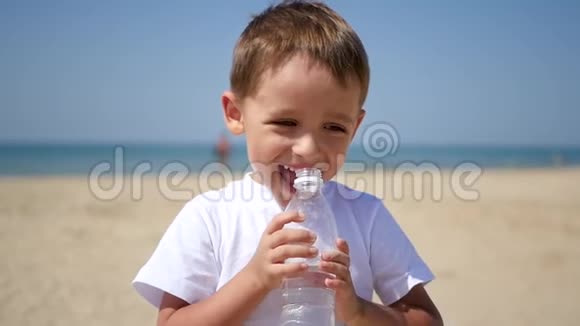 孩子从一个透明的塑料瓶子里喝水然后在沙滩上微笑视频的预览图