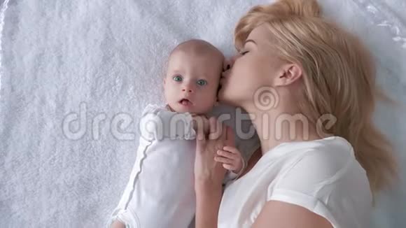 家庭和幸福慈爱的年轻母亲拥抱并亲吻一个躺在白色背景下的新生女儿视频的预览图