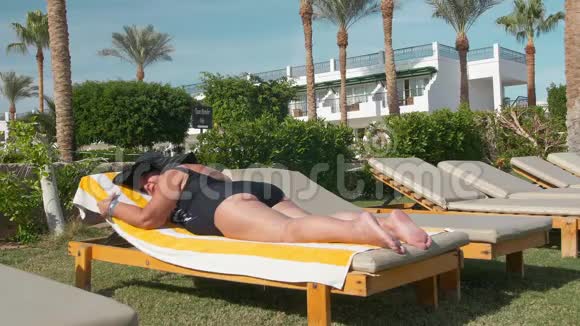 白种人老年女性戴着黑色帽子在阳光下晒太阳躺在一个阳光休息室在一个视频的预览图
