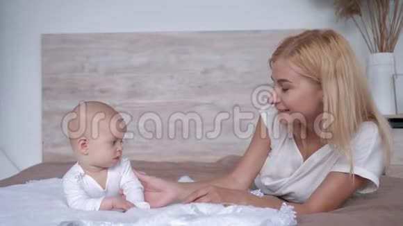 爱和幸福年轻的母亲和刚出生的小女孩一起躺在床上在家里看镜头视频的预览图