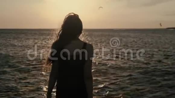一个年轻的女人在一天的日落时在风筝的背景下优雅地进入水中视频的预览图