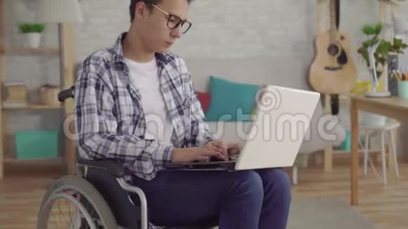 亚洲年轻男子戴着时髦的眼镜坐在轮椅上在视频的预览图