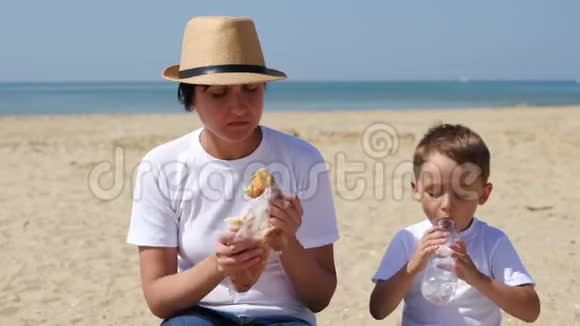 母亲和孩子坐在海边沙滩上吃喝视频的预览图