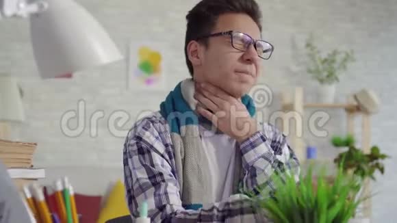 一个身穿衬衫的亚洲青年男子坐在笔记本电脑前用喷雾剂治疗喉咙痛视频的预览图