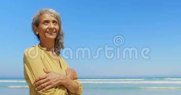 站在海滩上双臂交叉的快乐活跃的非裔美国妇女的正面景色视频的预览图