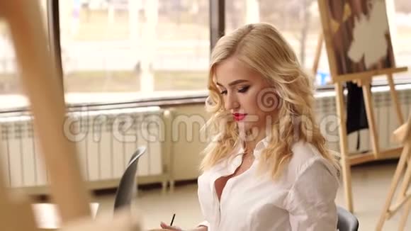 金发女孩红唇手里拿着画笔在画室里视频的预览图