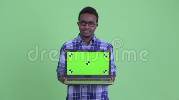 年轻快乐的非洲时髦男人一边思考一边展示笔记本电脑视频的预览图