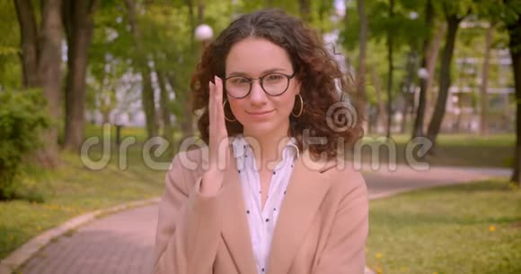 一位年轻的长头发的卷曲的白种人女学生的特写照片她开心地笑着端着眼镜看着视频的预览图
