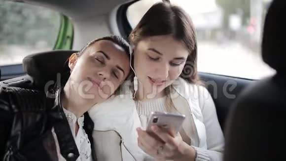 两个女朋友坐在后座的车里女孩睡着了把头放在朋友的肩膀上视频的预览图