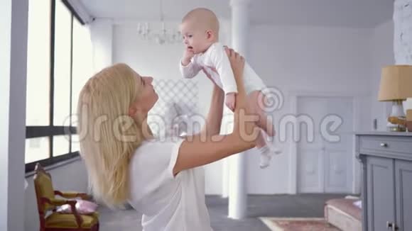 母子关系快乐的妈妈在甜蜜的婴儿女孩的头顶上用手指在嘴里玩耍视频的预览图
