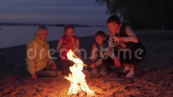 在夜间海滩野餐时一家人在火上吃饭和聊天视频的预览图