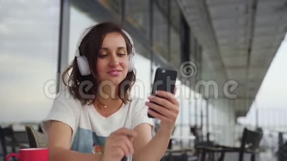 戴着耳机听音乐和在智能手机上聊天的年轻女性视频的预览图