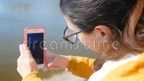 美丽的女孩用智能手机拍摄河流特写镜头秋季天气晴朗视频的预览图
