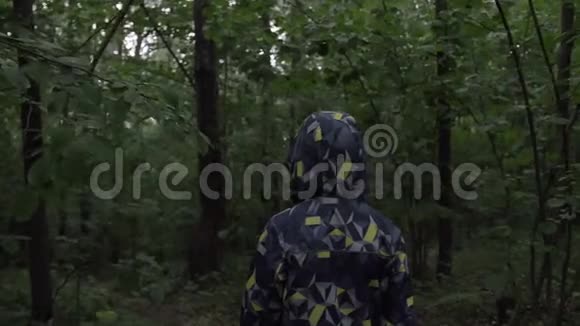晚上穿着夹克和兜帽的男孩穿过森林视频的预览图