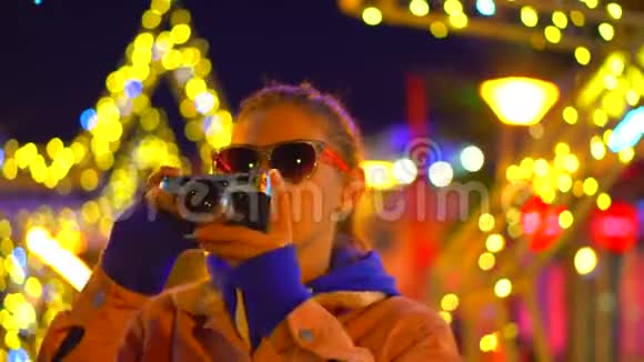 一个戴眼镜的女孩站在城市灯光下的霓虹灯中用摄像机拍摄视频的预览图