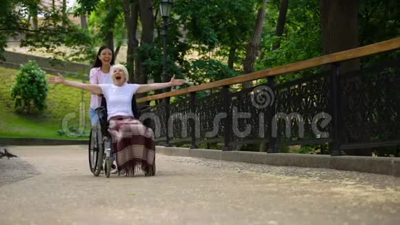 快乐志愿者推轮椅与积极的老太太快乐的女性病人视频的预览图