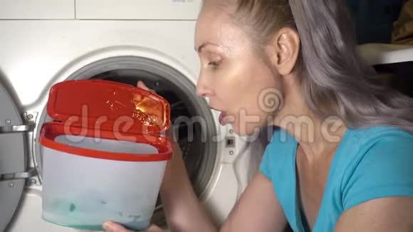 年轻女子准备在洗衣机里洗衣服拿出并打开装有洗衣粉的盒子视频的预览图